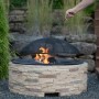 Westmann Feuerstelle in Steinoptik mit Funkenschutzgitter und brennendem Feuer im Garten.