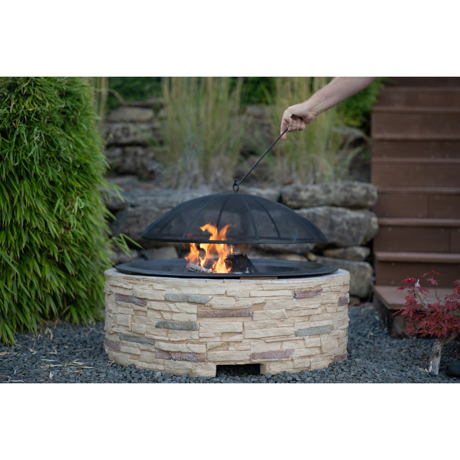 Westmann Feuerstelle in Steinoptik mit Funkenschutzgitter und brennendem Feuer im Garten.