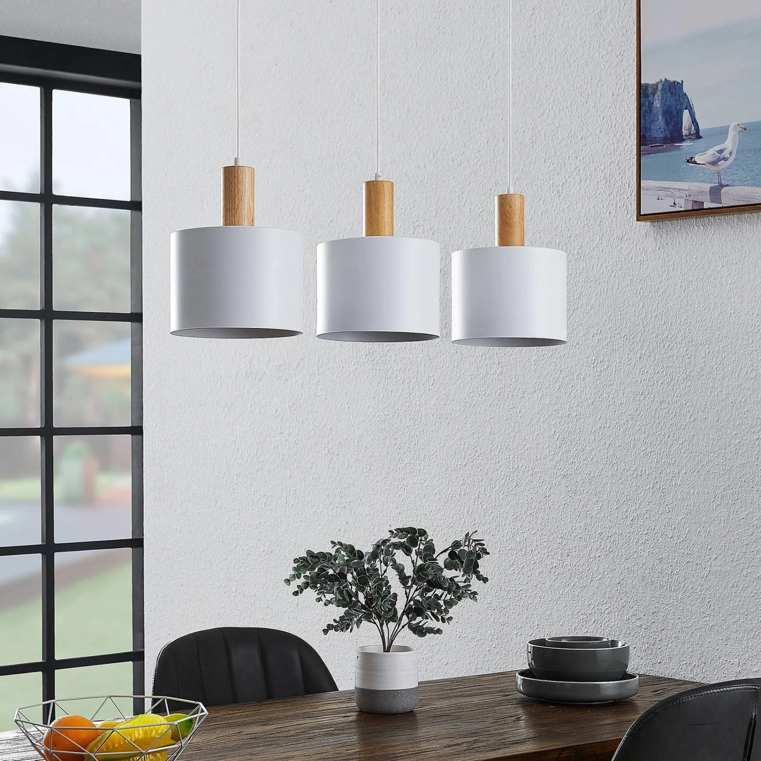 Moderne Lindby Pendelleuchte Kadir, weißes Metall, 3-flammig, mit Holzdetails über einem Esstisch.