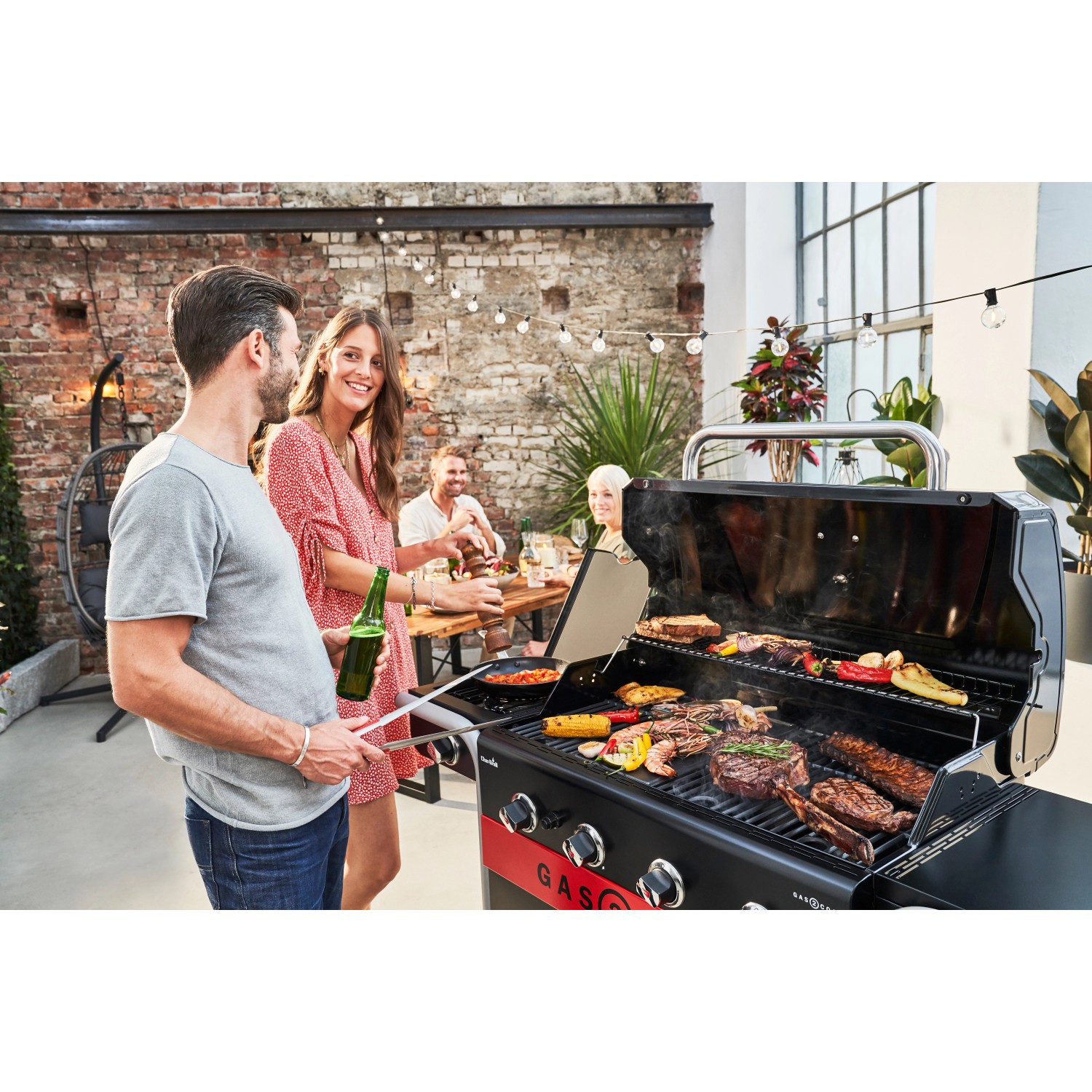 Char-Broil Gas2Coal 2.0 Hybridgrill mit Grillgut und Personen im Garten.