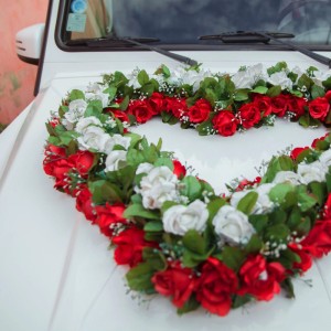 Herzförmiges Gesteck aus roten und weißen Kunstrosen auf weißem Auto. Ideal für Hochzeitsdeko mit roten Polyester-Rosen.
