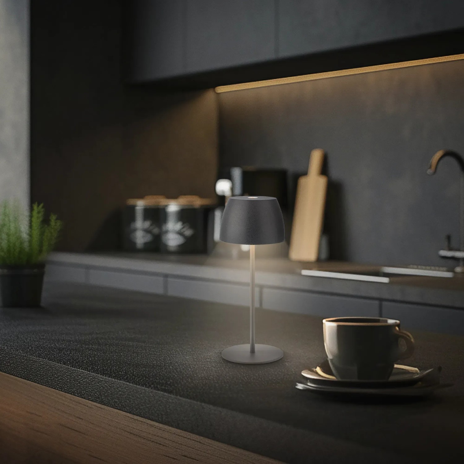 Anthrazitfarbene Brilo LED Akku-Tischleuchte Serina Mini (20 cm) auf dunkler Arbeitsfläche.