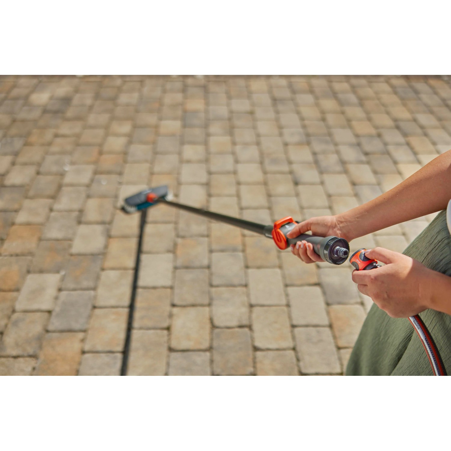 Gardena Cleansystem Stielbürste Hard mit Schlauchanschluss im Einsatz zur Reinigung von Pflastersteinen.