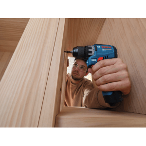 Mann bohrt mit Bosch PRO Akku-Bohrschrauber GSR 12V-31 in Holz. Ideal für enge Bereiche durch 144 mm Kopflänge.