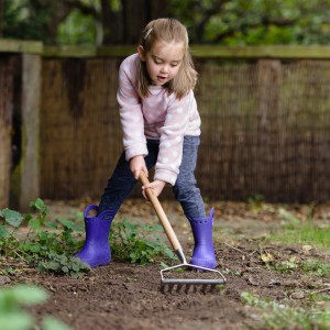 Mädchen harkt mit dem Kent & Stowe Kinder-Gartenrechen den Garten.