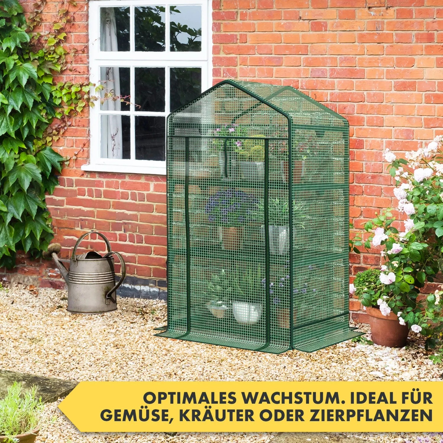 Grünes KARAT Gewächshaus Bloom mit 3 Ebenen, Gitteroptik, vor einer Backsteinmauer mit Fenster.