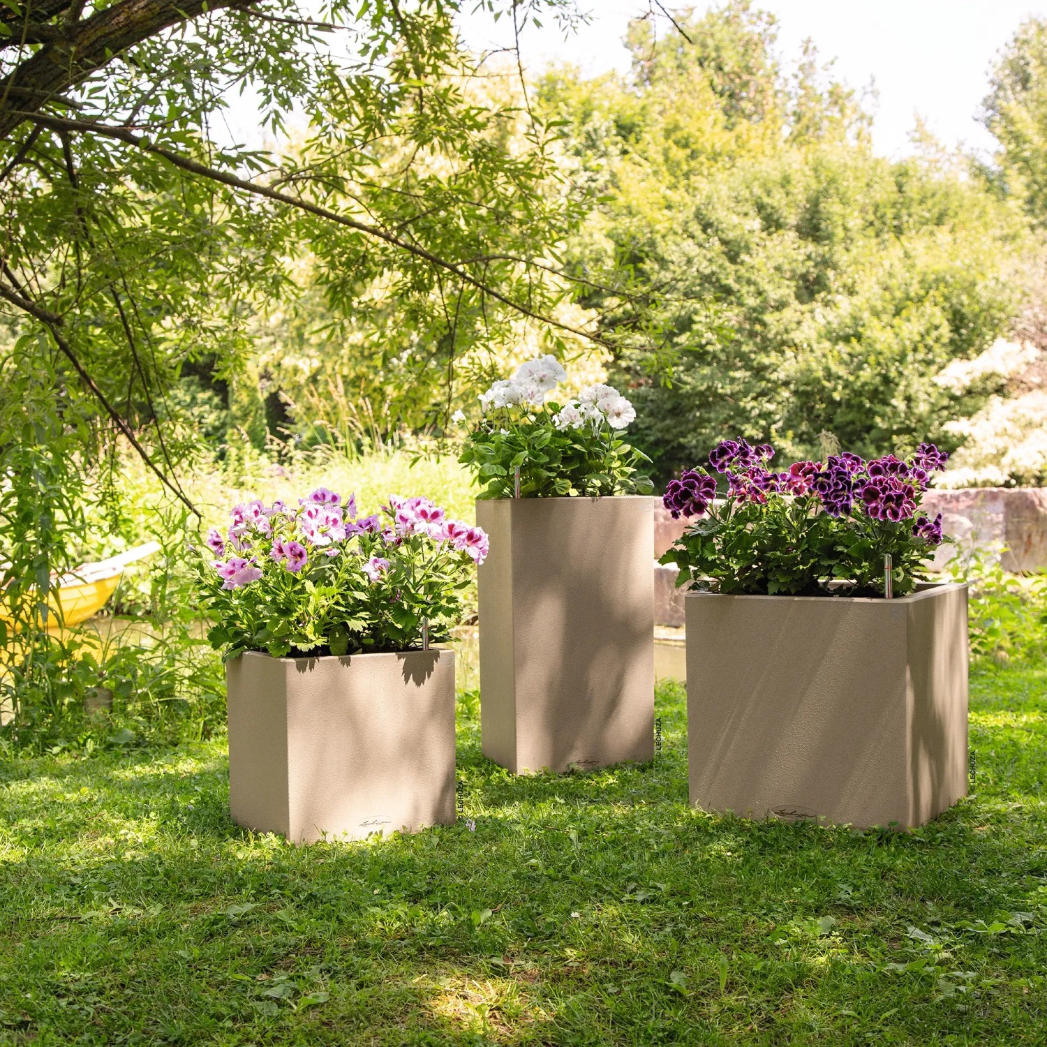 Lechuza Canto Stone Pflanzsäulen, sandbeige, mit bunten Blumen bepflanzt im Garten.