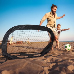 Schwarzes Relaxdays Fußballtor mit Torwand, spielende Familie am Strand.