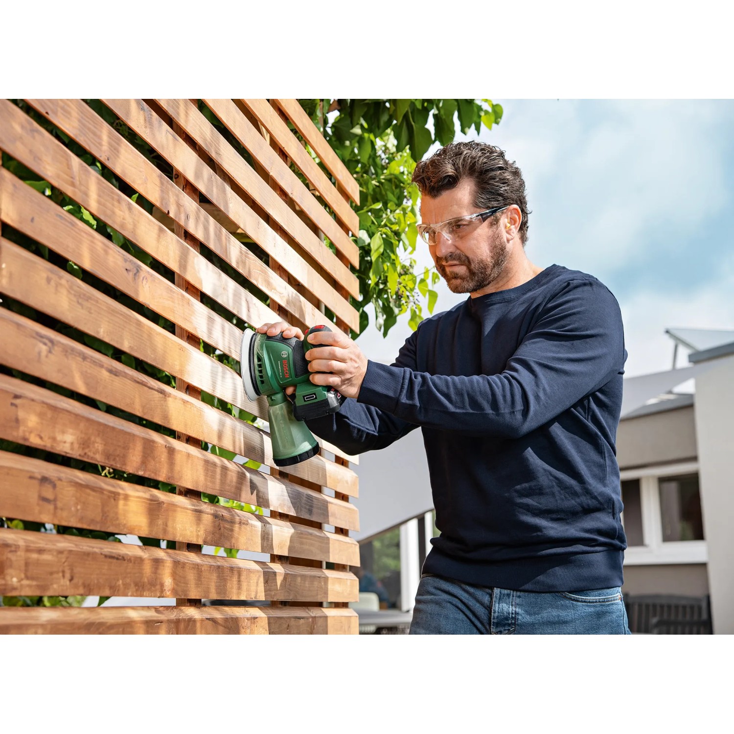 Mann schleift Holz mit Bosch Akku-Exzenterschleifer UniversalOrbit 18V-20. Schleifmaschine für Heimwerker.