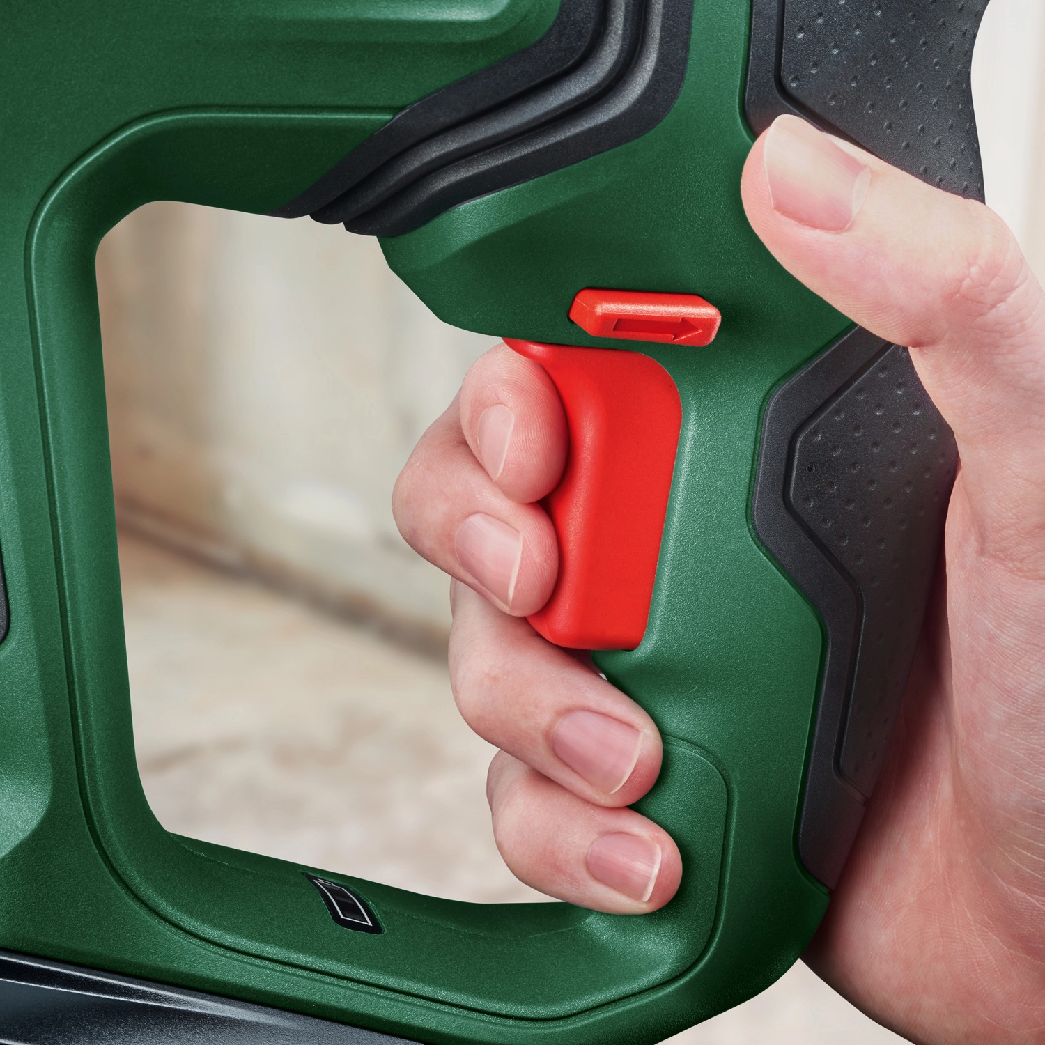 Detailaufnahme: Hand betätigt roten Auslöser am grünen Bosch Akku-Bohrhammer UniversalHammer 18V.