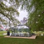 Juliana Gewächshaus Grand Oase 18 Anthrazit im Garten mit Teich und Haus im Hintergrund.