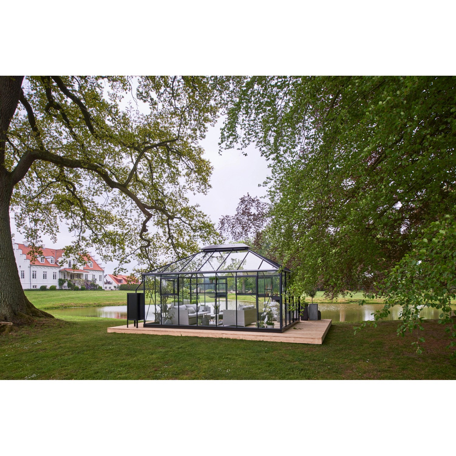 Juliana Gewächshaus Grand Oase 18 Anthrazit im Garten mit Teich und Haus im Hintergrund.