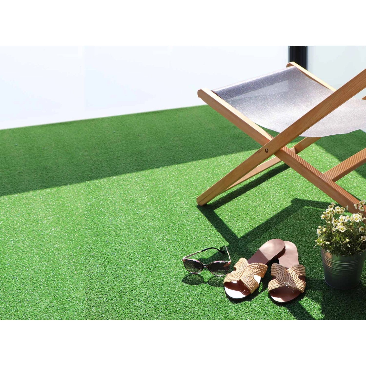 Grüner Primaflor Kunstrasen Wimbledon auf Balkon mit Liegestuhl, Schuhen und Pflanze.