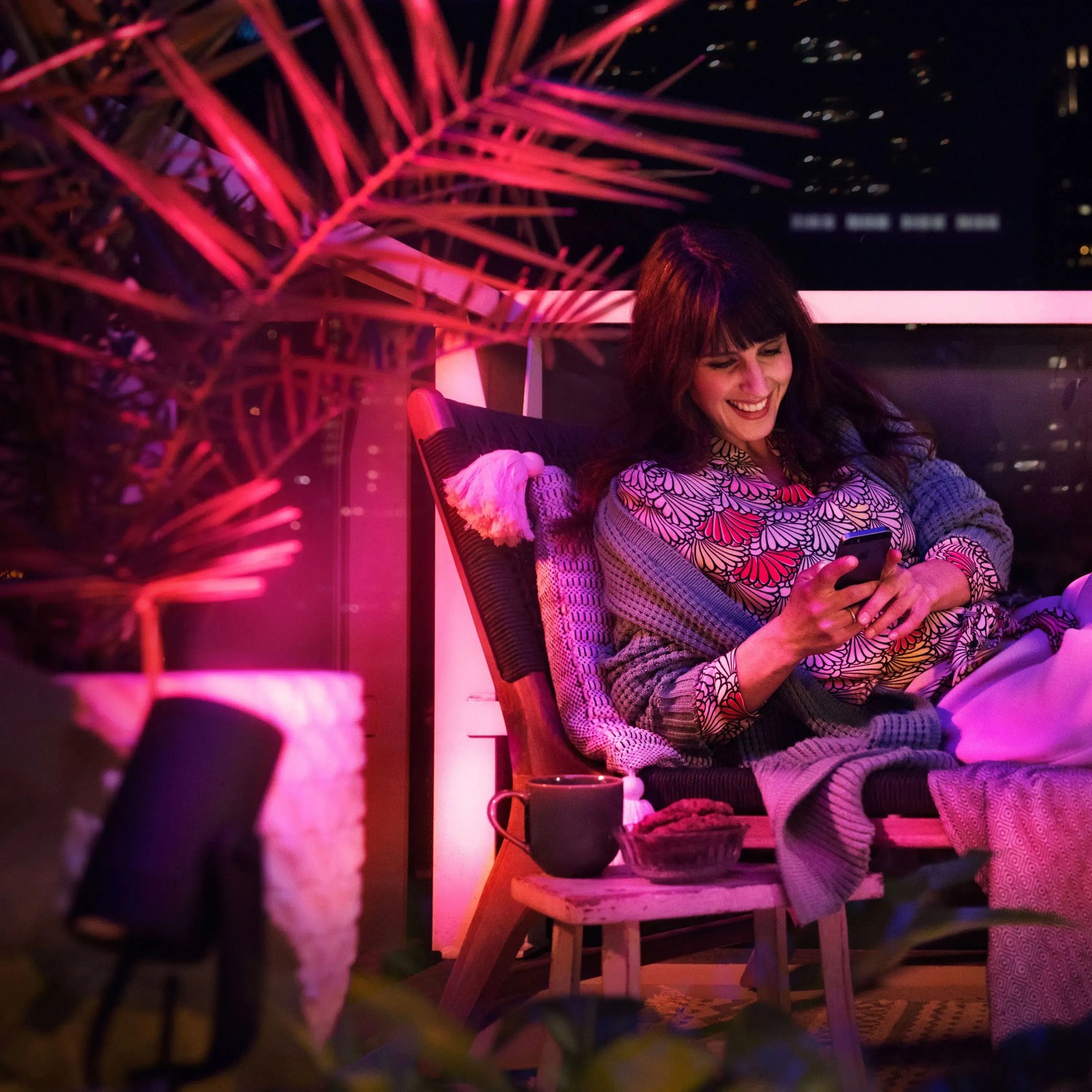 Philips Hue Lily Spot Basis-Set: Frau entspannt im farbig beleuchteten Garten mit der smarten Außenleuchte.