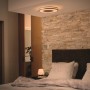 Philips Hue Being Deckenleuchte in Silber, montiert in einem Schlafzimmer mit Steinwand.