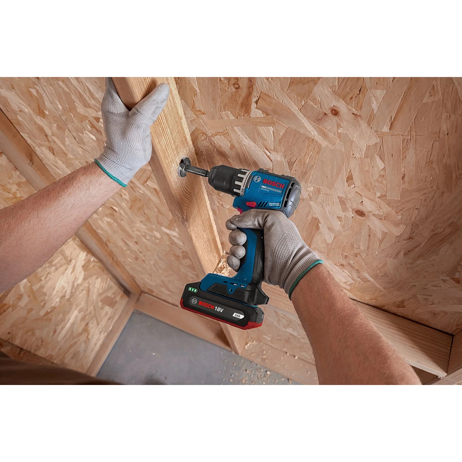 Blauer Bosch Professional Akku-Bohrschrauber GSR18V-52 bohrt in Holz. Hände mit Handschuhen halten den 18V Akkuschrauber.