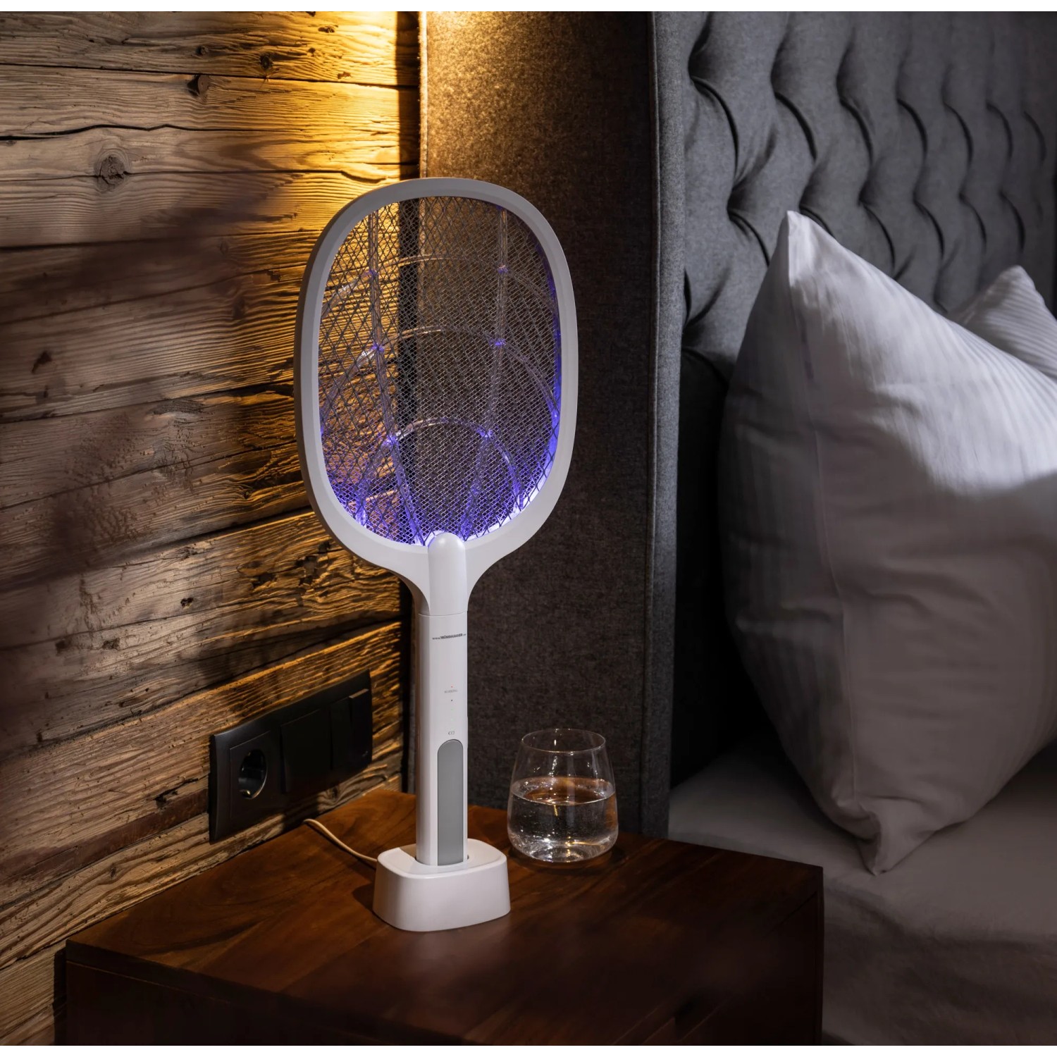 Windhager Fliegenklatsche 2-in-1 elektrisch mit UV-Licht in Ladestation auf Nachttisch.