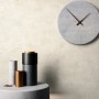 Cremefarbene Vliestapete mit Betonstruktur an einer Wand, dekoriert mit Uhr und modernen Vasen. Für ein edles Raumgefühl.
