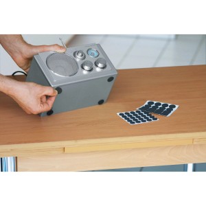 Schwarze, klebende Rutschstopper unter einem Radio, Möbelgleiter auf Bögen auf Tisch.