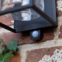 Schwarze, eckige Lutec Solar-Wandleuchte Flair mit Bewegungsmelder an einer Backsteinwand.