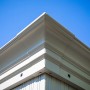 Detailaufnahme: Ecke des champagnerfarbenen Sojag Striano Pavillons mit Stahldach vor blauem Himmel.