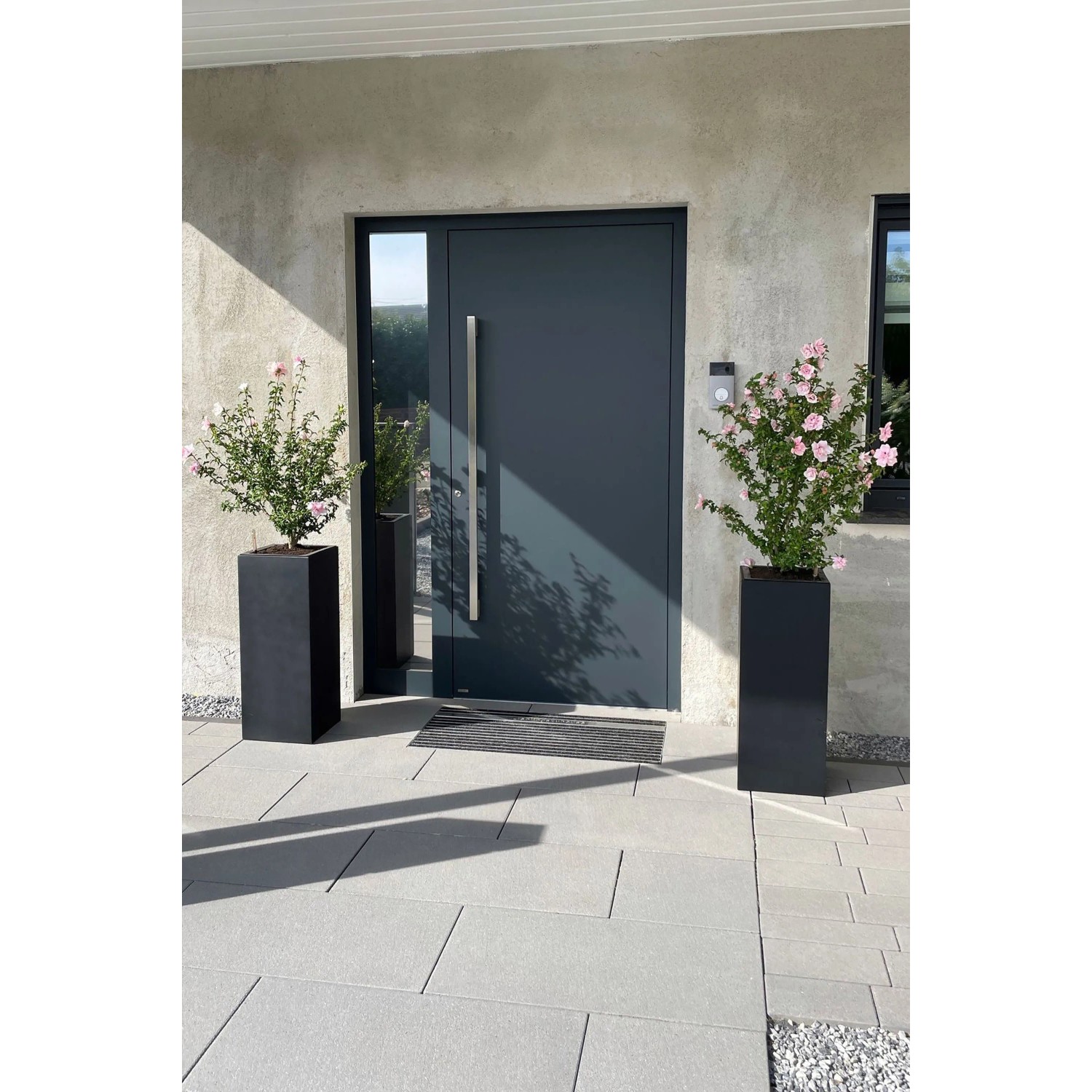 Anthrazitfarbener Vivanno Pflanzkübel Block (30x30x75 cm) mit Bepflanzung vor einer Haustür.