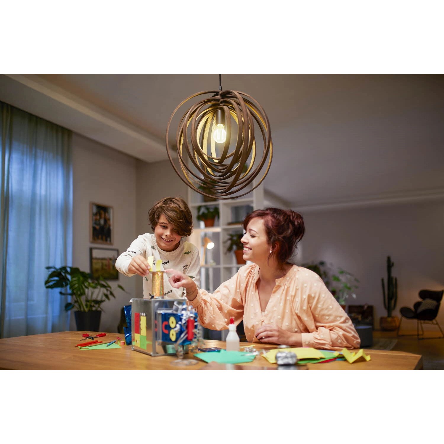 Philips LED E27 Lampe, 4W, klare Glühlampenform unter einer modernen Hängelampe im Wohnzimmer.