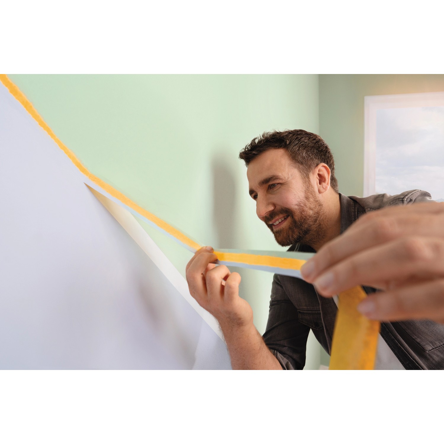 Mann klebt tesa® Malerband Perfect+ an eine Wand für scharfe Farbkanten.