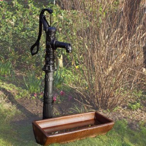 Schwarze TRUTZHOLM Schwengelpumpe aus Gusseisen mit Ständer im Garten.