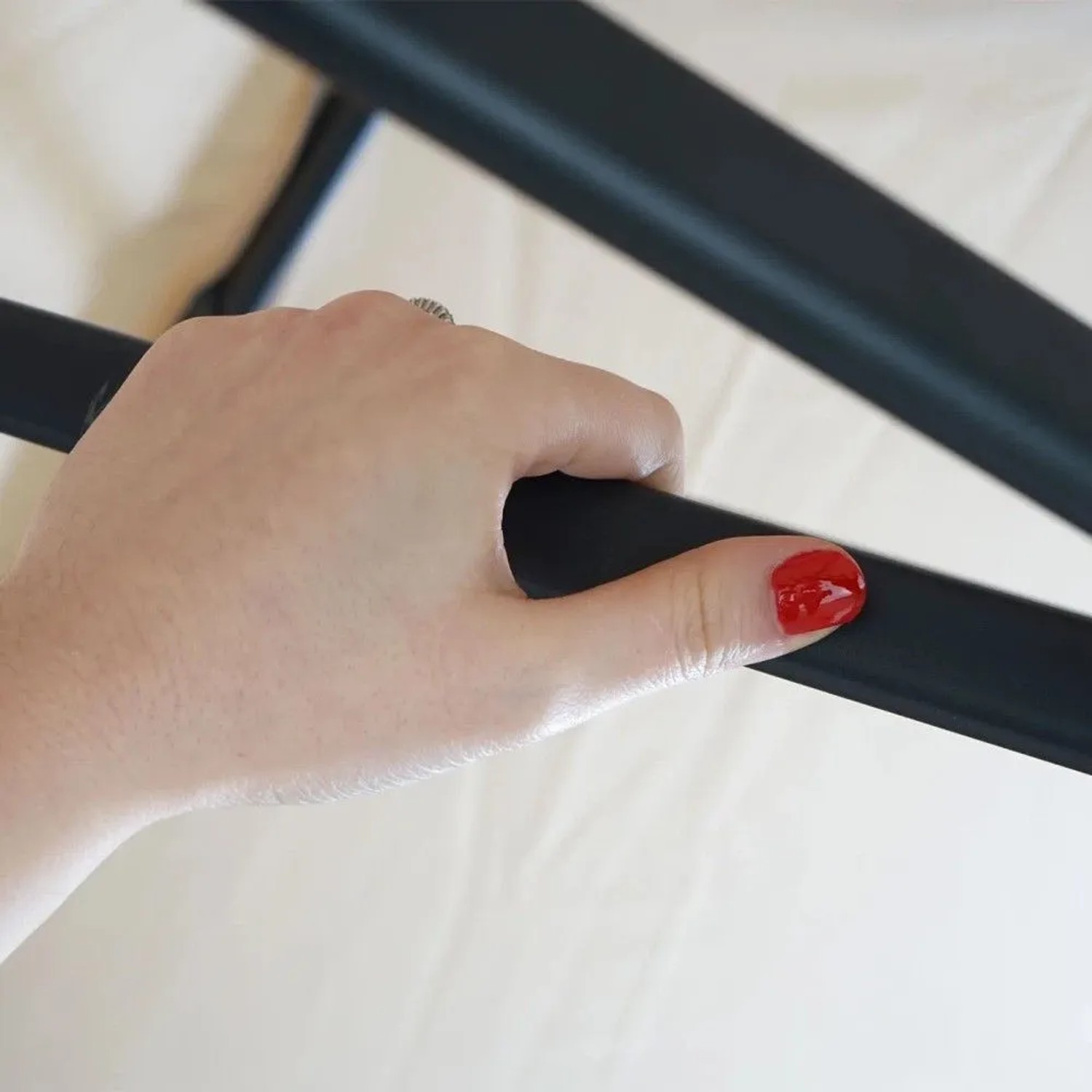 Hand greift dunkle Stahlstrebe des cremefarbenen Ampelschirms. Detail des robusten Mastes und Bezugs.