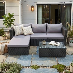 SVITA QUEENS Gartenlounge Set: schwarzes Polyrattan Sofa, Hocker, Glastisch mit grauen Kissen auf Terrasse.