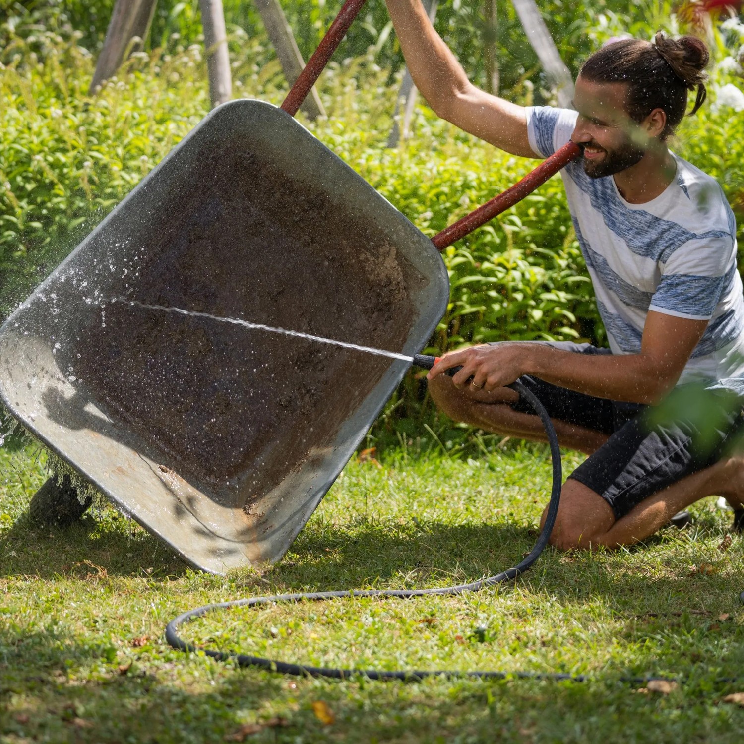 Mann reinigt Schubkarre mit Wasserstrahl im Garten. Gardena Haus- und Gartenautomat 5000 Silent Comfort.
