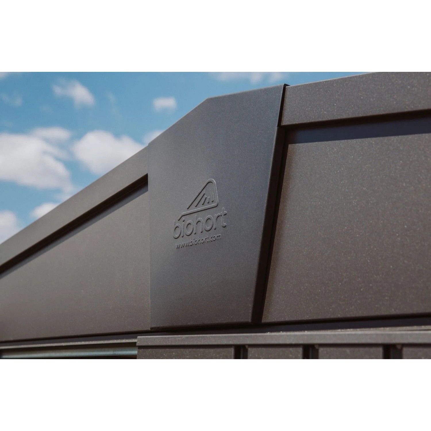 Biohort Metall-Gerätehaus Europa, dunkelgrau-metallic. Robuste Metallwand mit Biohort Logo vor blauem Himmel.