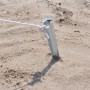 Silberfarbener V-förmiger Zelt-Hering aus verzinktem Stahl im Sand, mit weißem Seil befestigt. Für sicheren Halt beim Camping.