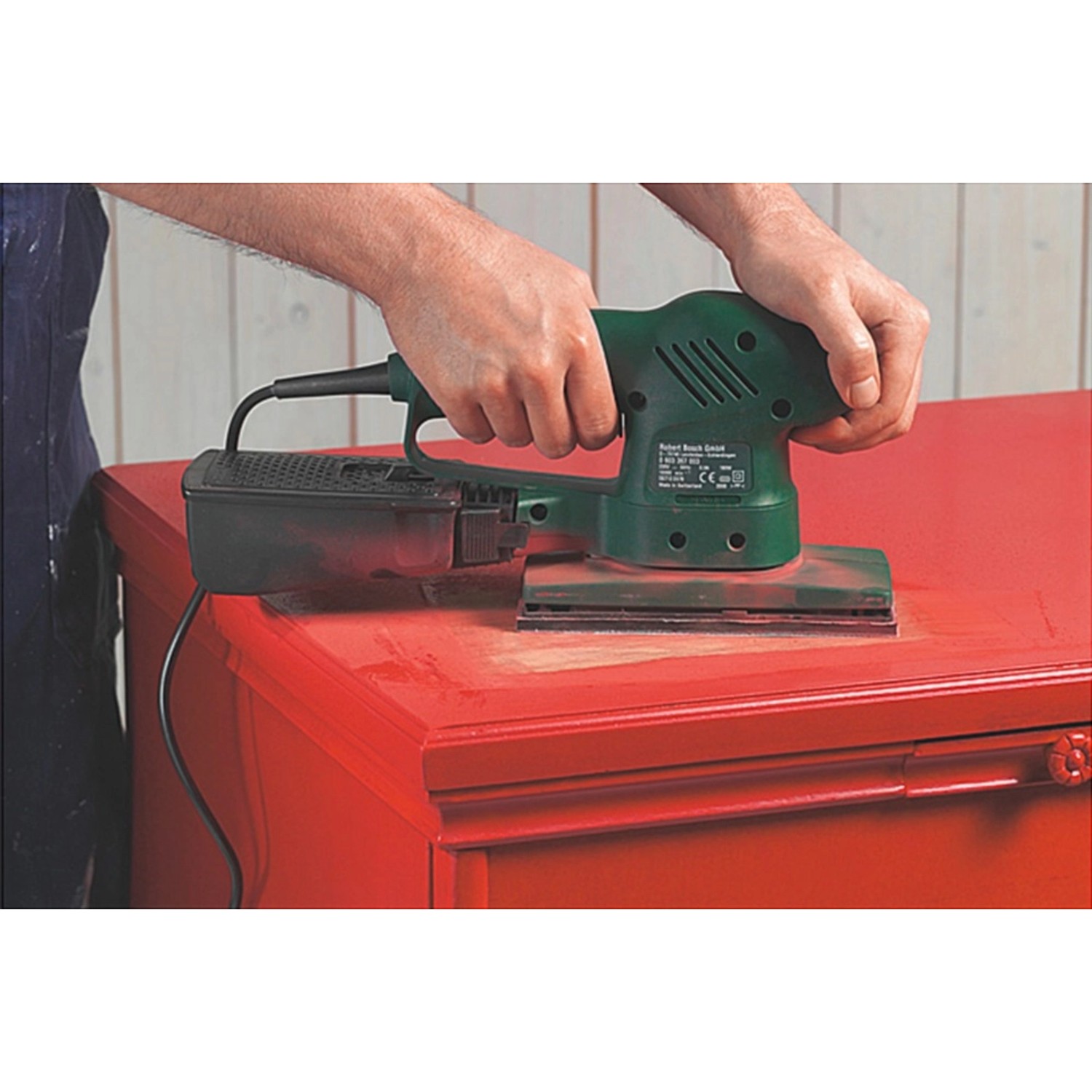 Schwingschleifer mit Schleifstreifen beim Bearbeiten eines roten Holzmöbels.