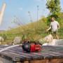 Einhell Aquinna Akku-Gartenpumpe auf Holzsteg, Mann bewässert Garten. Elektro-Pumpe für flexible Gartenbewässerung.