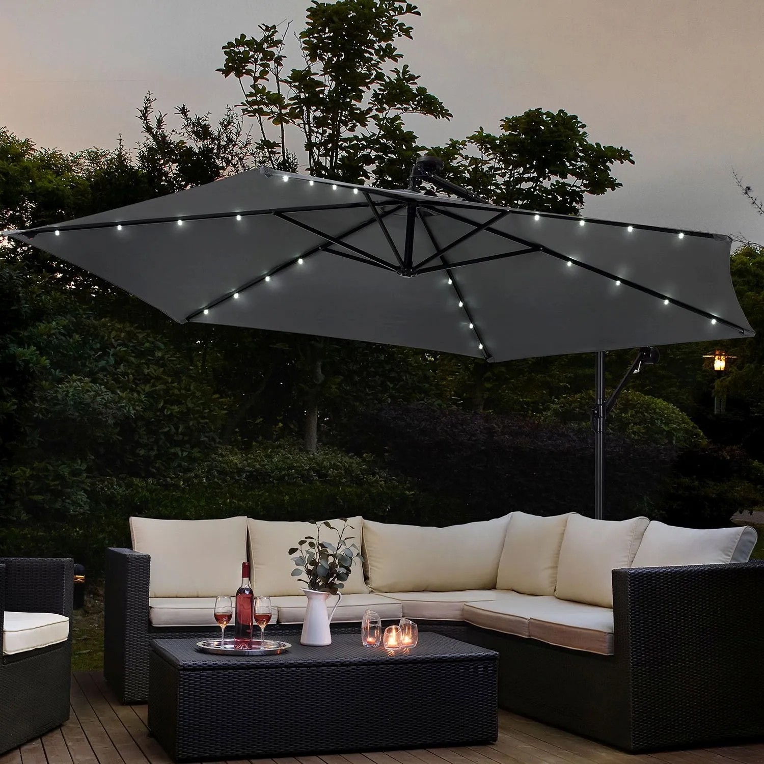 Grauer Juskys Ampelschirm Brazil Ø 3,5m mit LED, Kurbel und Standfuß über einer Loungegruppe.