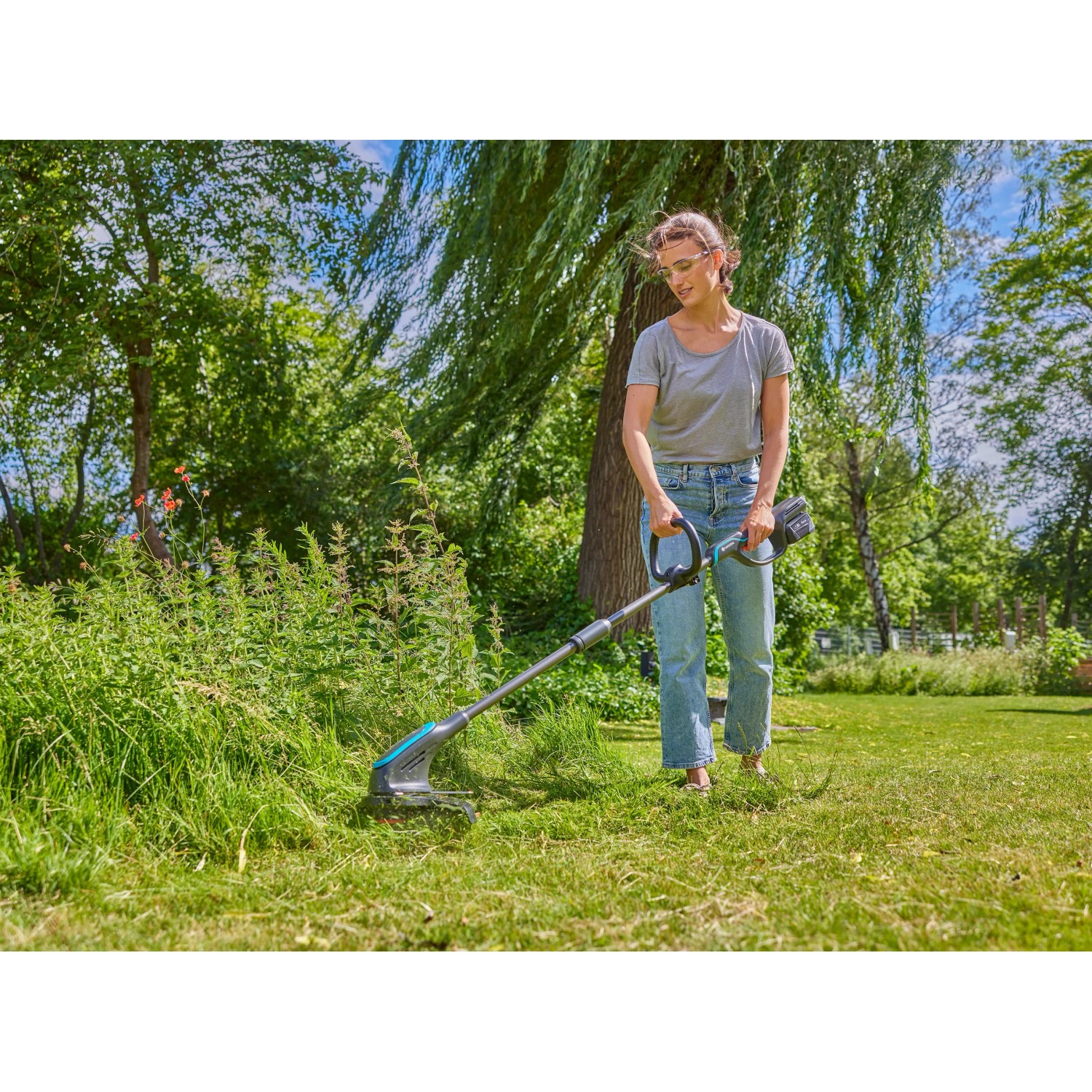 Frau trimmt Rasen mit Gardena Akku-Rasentrimmer PowerTrim 30/18V. Akku-Trimmer im Einsatz.