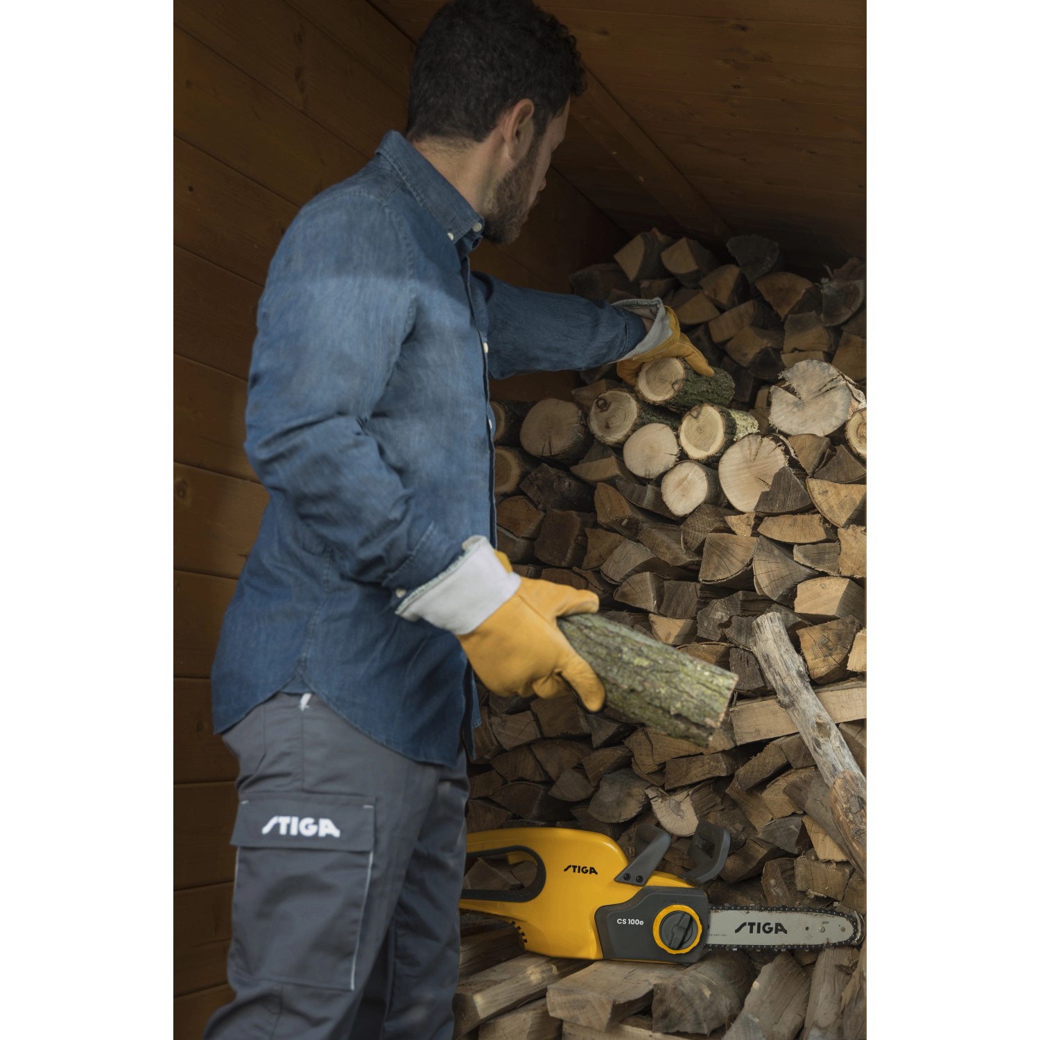 Mann lagert Holz neben Stiga Akku-Kettensäge CS 100e. Inkl. Akku.
