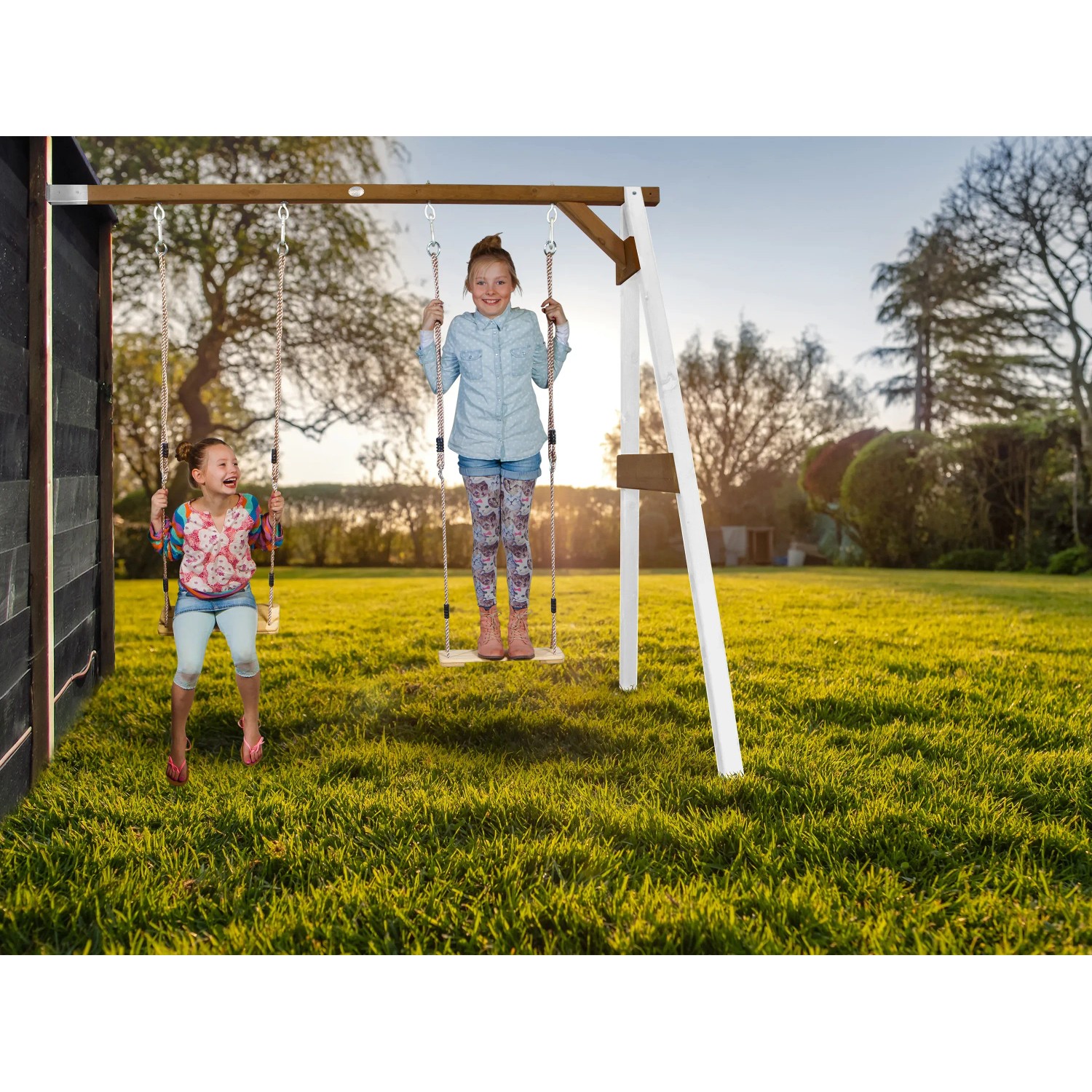 Axi Doppel-Anbauschaukel aus Holz in Weiß und Braun mit zwei Kindern beim Schaukeln im Garten.