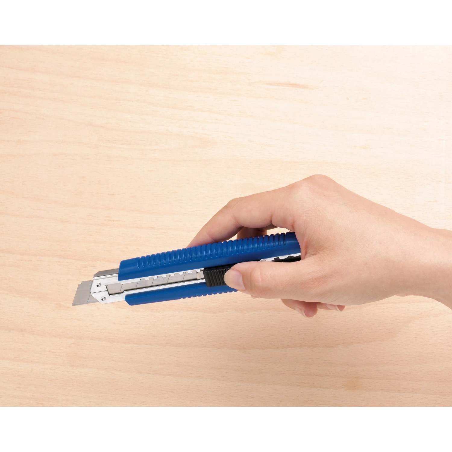 Hand hält blaues LUX Cuttermesser Classic 100 mm vor hellem Holzgrund.
