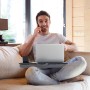 Mann auf Sofa mit grauem Relaxdays Laptopkissen, Laptop und Handyhalterung. Bequemes Arbeiten im Bürobedarf.
