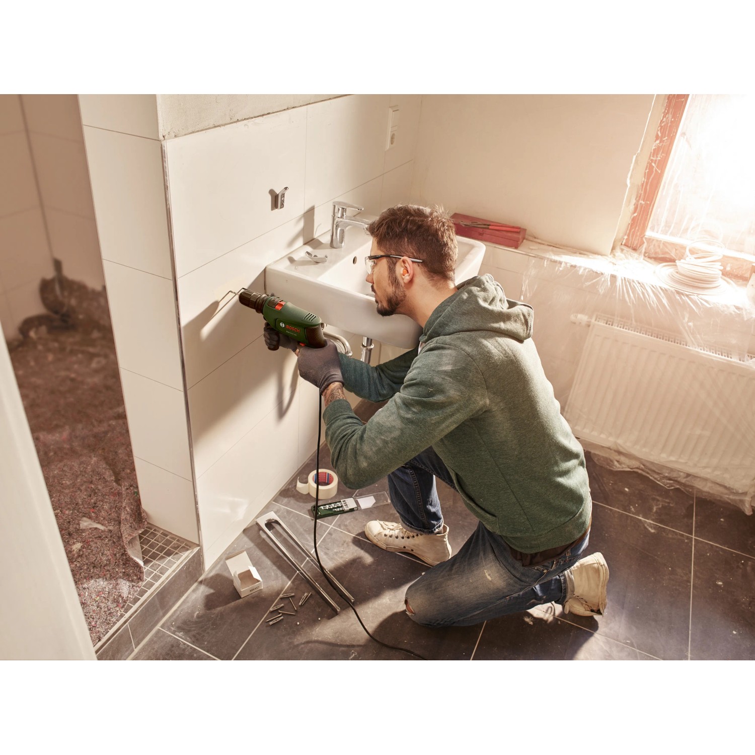 Mann bohrt mit Bosch EasyImpact 600 Schlagbohrmaschine in Fliese im Bad.