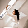 Frau bedient weißen VELUX Faltstore FHL S08 am Dachfenster.