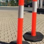 Zwei orange UvV FLEX Absperrpfosten mit Reflexstreifen und schwarzer Fußplatte.