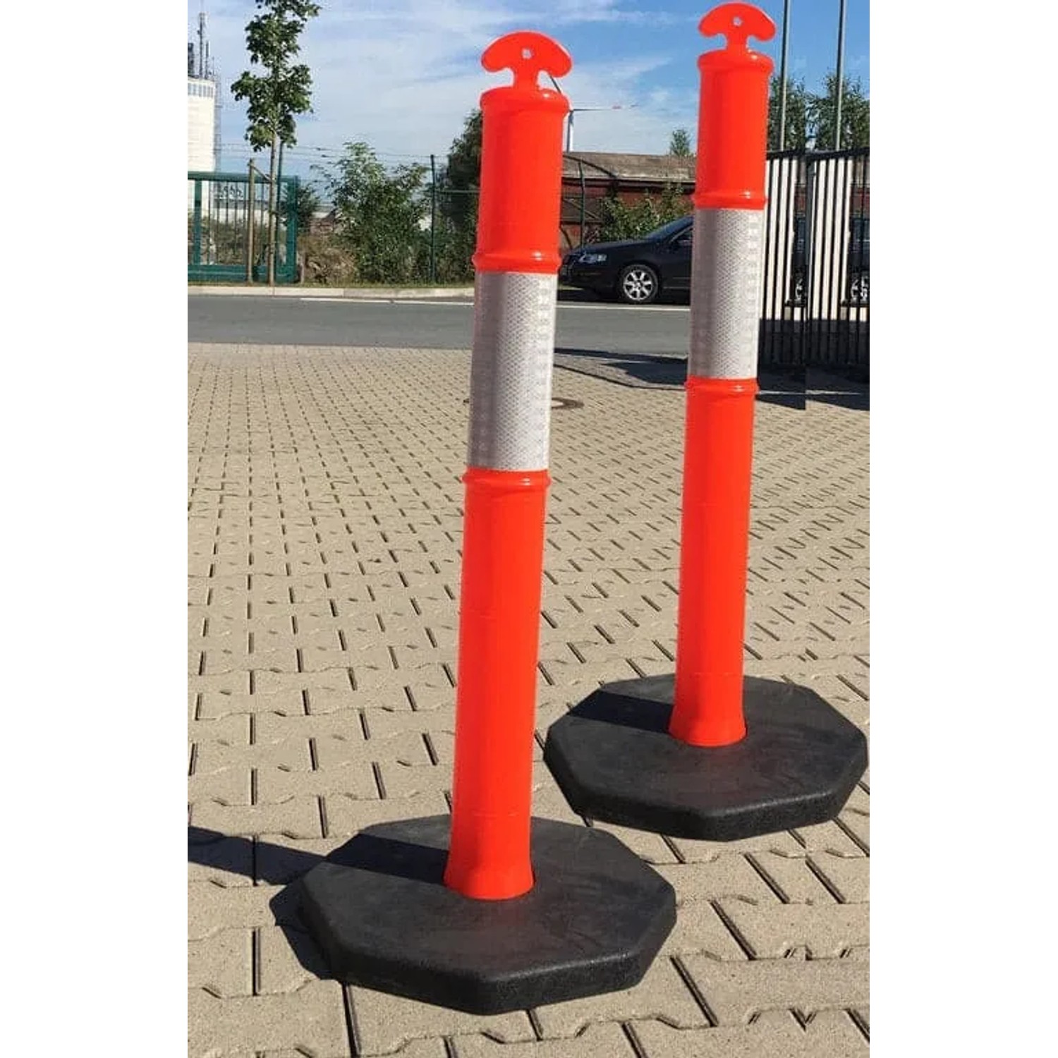 Zwei orange UvV FLEX Absperrpfosten mit Reflexstreifen und schwarzer Fußplatte.