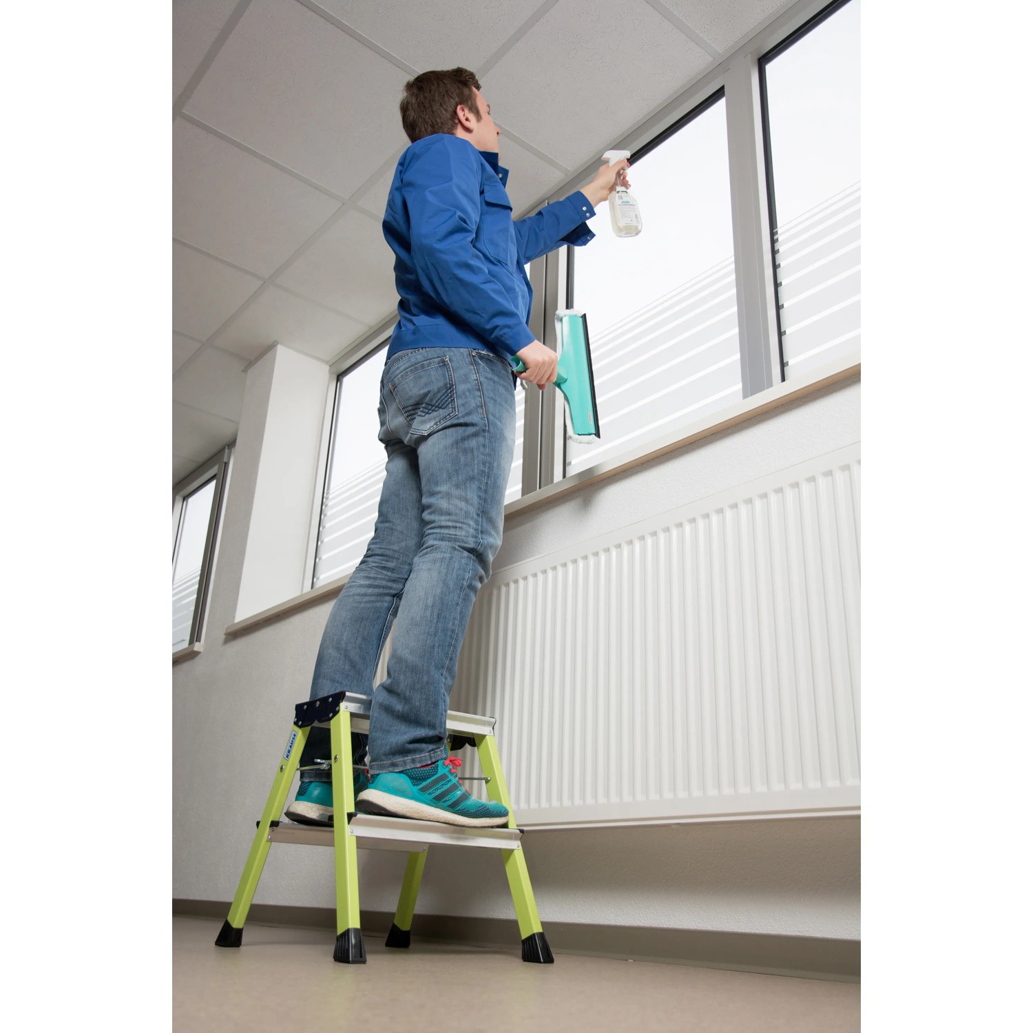 Mann reinigt Fenster stehend auf Krause Klapptritt Rolly, grün. Leiter mit 2 Stufen.