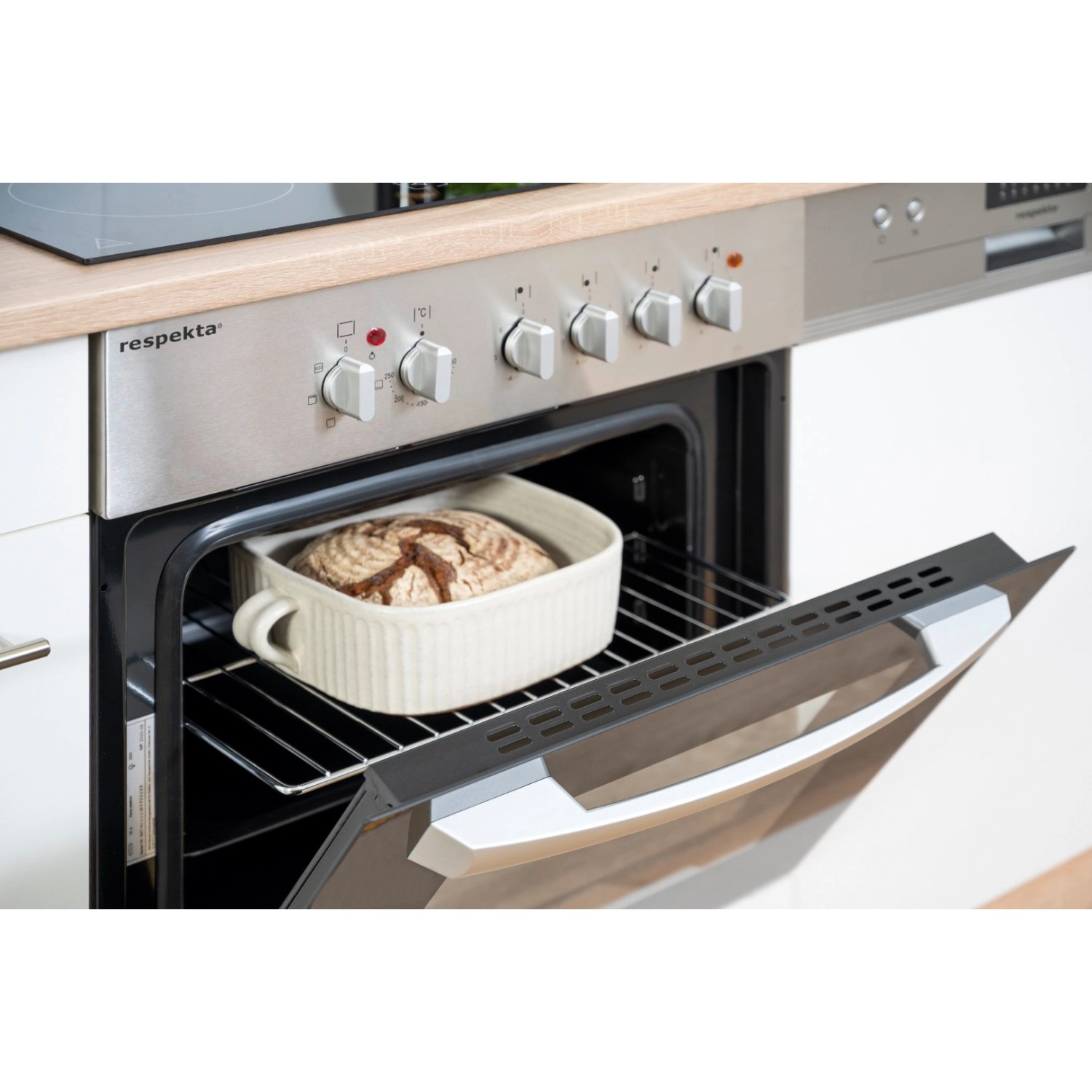 Respekta Küchenzeile: Brotbacken im Ofen. Weißer Ofen mit Brot in Keramikform. Teil einer modernen Einbauküche.