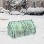 Grünes Foliengewächshaus mit Metallrahmen und Pflanzen im verschneiten Garten. Bietet Schutz vor Kälte und Frost.