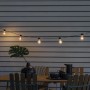 Konstsmide LED Biergarten Lichterkette mit 10 bernsteinfarbenen Leuchtmitteln über einem Gartentisch.